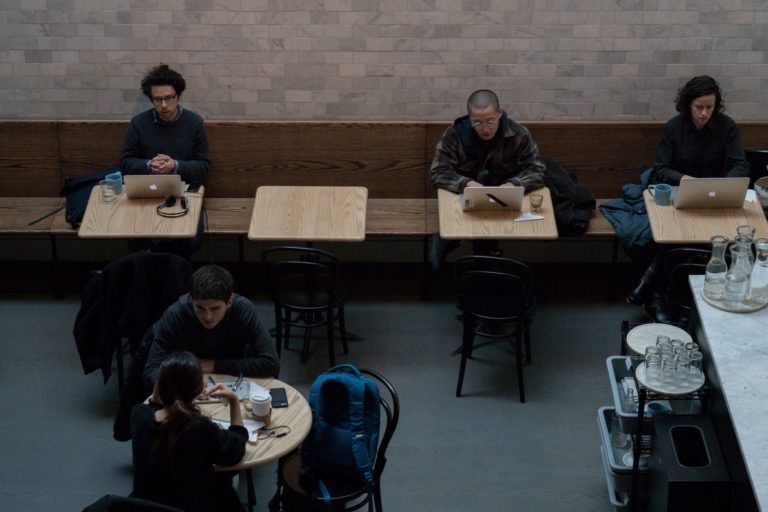 Photo taken from a raised view showing people working in a coffee shop, on laptops.